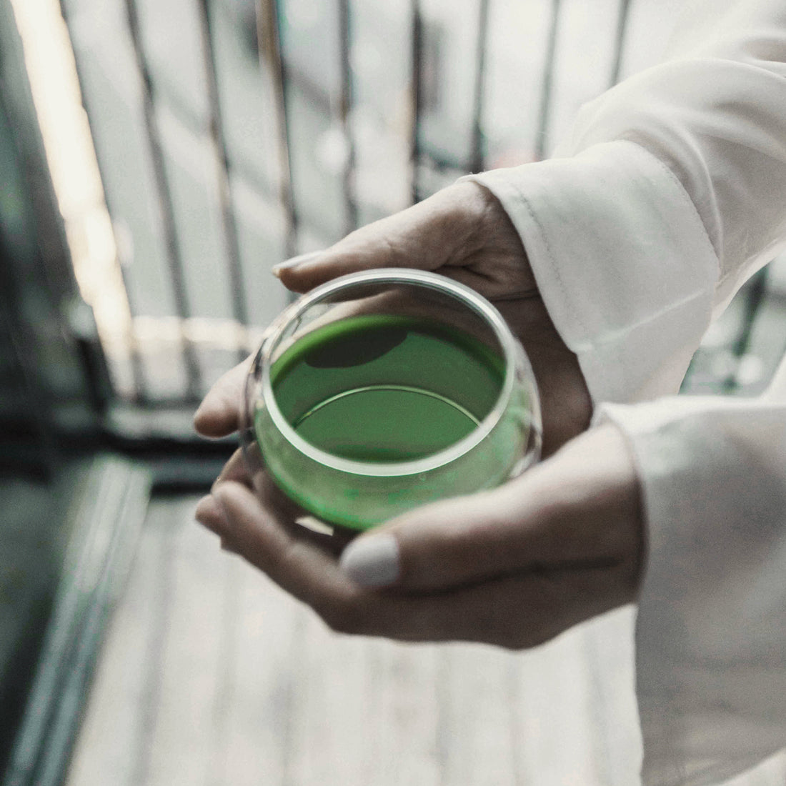 Mains tenant délicatement un bol en verre transparent rempli de matcha d’un vert vibrant, symbolisant un moment de tranquillité et de bien-être.